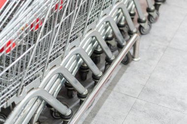 Bir perakende mağazasında yığılmış alışveriş arabalarının yakın çekim görüntüsü, fayanslı zeminde metalik çerçevelerini ve tekerleklerini sergiliyorlar..