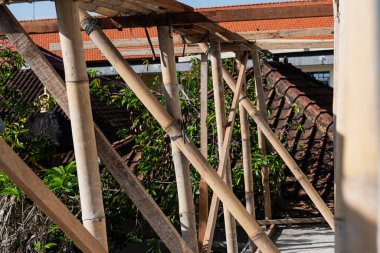 Geleneksel fayanslı çatı zeminine karşı bambu iskelesinin yakın çekim görüntüsü. Güneş ışığı, bambunun üzerine gölgeler düşürür. Doğal dokusunu ve çevresini aydınlatır.
