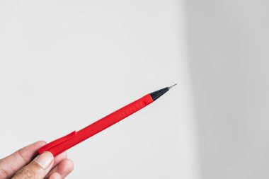 Siyah uçlu kırmızı kalemi arka planda tutan biri. Kalem belirgin bir şekilde gösterilir, tasarımı ve rengi gösterilir.