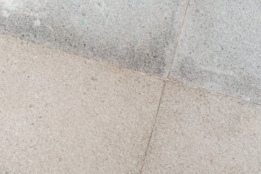 Betona gömülü küçük çakıl taşlarından oluşan bir desen içeren dokulu taş kaldırımın yakın çekim görüntüsü. Güneş ışığı yüzeyde gölgeler oluşturur, pürüzsüz ve pürüzsüz arasındaki zıtlığı vurgular.