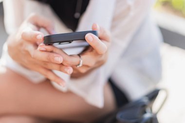 Ekrana odaklanmış, akıllı bir telefonu tutan birinin yakın plan fotoğrafı. El renkli bir bilezikle süslenmiş ve arka plan hafifçe bulanıklaşmış..
