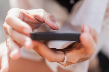 Ekrana odaklanmış, akıllı bir telefonu tutan birinin yakın plan fotoğrafı. El renkli bir bilezikle süslenmiş ve arka plan hafifçe bulanıklaşmış..