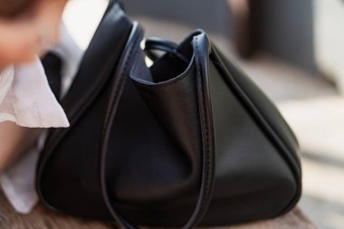 Ahşap bir yüzey üzerinde duran şık siyah deri bir çantanın yakın çekim görüntüsü. Poşette yumuşak kıvrımlı ve minimalist estetik bir tasarım yer alıyor. Yüksek kaliteli malzemeler sergiliyor.