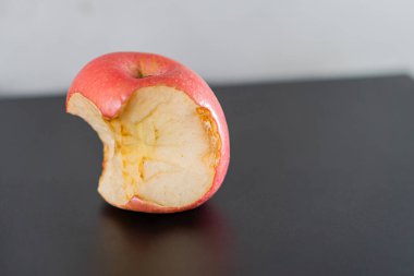 İçini gösteren, kısmen yenmiş kırmızı bir elma, içinden bir ısırık alınmış. Elma, siyah bir yüzeye yerleştirilir, arkaplan rengini ve dokusunu vurgulayan nötr bir altyapıya sahiptir..