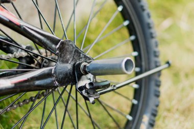 Motosikletin arka tekerleğinin ve mandalının detaylı görünümü, mekanik parçaları ve dokuları vurguluyor, doğal bir arkaplana karşı ayarlanıyor.