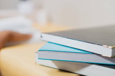 Tahta bir masanın üzerine istiflenmiş üç kitabın yakın plan fotoğrafı. Yumuşak doğal ışıklandırmayla sessiz bir çalışma ortamını mükemmel bir şekilde yakalıyor. Eğitim ve öğrenme temalı kavramlar için ideal.