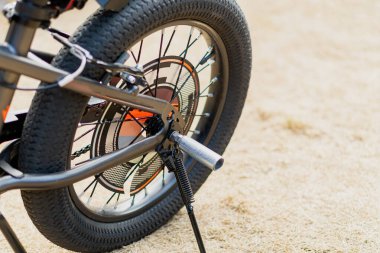 Kumlu zeminde bir kickstand bulunan modern bir bisiklet tekerleğinin ayrıntılı görüntüsü. Bisiklet, macera ve sürdürülebilir ulaşım kavramları için mükemmel..