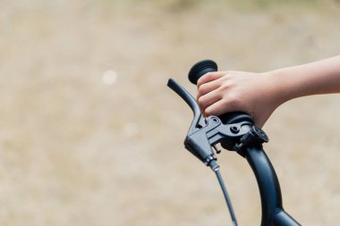 Bir çocuğun eli bisiklet gidonunu sıkıca kavrıyor, açık havada bisiklet sürmenin ve doğal ortamdaki maceranın heyecanını sergiliyor..