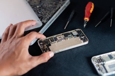 Masadaki aletlerle akıllı bir telefonu tamir eden bir kişi.