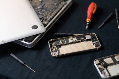 Parçalanmış bir akıllı telefon ve dizüstü bilgisayarın karanlık bir yüzey üzerinde araçları ile yakın plan görüntüsü.