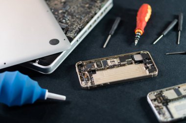 Karanlık bir yüzeyde tamir aletleri olan parçalanmış bir akıllı telefon ve dizüstü bilgisayar..