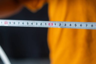 Bulanık bir arka planı olan birinin elinde tutulan bir ölçüm bandının yakın çekimi. Bu bant santimetre ve inç cinsinden ölçümleri gösteriyor, hassasiyeti ve ölçümü gösteriyor.