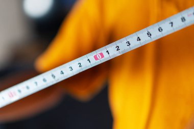 Turuncu tişört giyen birinin elinde tuttuğu bir mezura. Kaset, rakamlara odaklanarak ölçümleri açıkça gösteriyor..