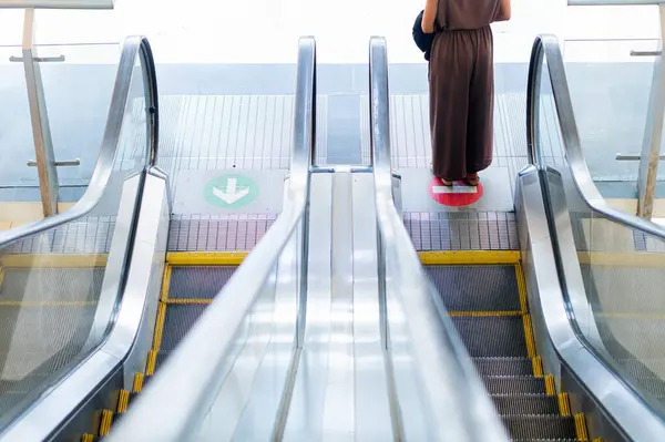 Yürüyen merdivenin üstünde duran, yukarıdan bakan biri. Yürüyen merdivenin üzerinde yeşil oklar ve kırmızı daire iddianamesi olan açık bir yön göstergesi var.