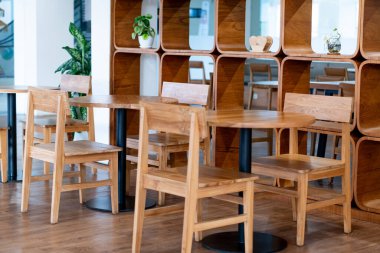 İçinde ahşap masalar ve sandalyeler olan modern bir kafe. Tasarım, aynaları ve dekoratif bitkileri olan ahşap bir raf ünitesini içeriyor. Atmosfer parlak ve net.