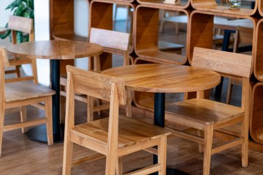 İçinde ahşap masalar ve sandalyeler olan rahat bir kafe. Masalar yuvarlak ve dikdörtgen, açık renkli ahşaptan yapılmış, siyah metal bazlı. Arkaplan gösterisi
