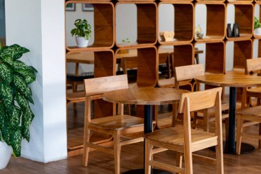 İçinde ahşap masalar ve sandalyeler olan rahat bir kafe. Tasarım, arka planda bitki ve dekoratif eşyalarla süslenmiş ahşap bir raf ünitesini içeriyor. Atomlar