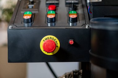 Acil stop düğmesi de dahil olmak üzere çeşitli düğmelerden oluşan bir kontrol panelinin yakın çekimi. Panelde yeşil, turuncu ve siyah renkli düğmeler var.