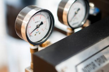 Bir makinedeki basınç göstergelerine yakın çekim, psi ve sırt tarağı ölçümlerini gösteriyor. Ölçümler metalik bir kaplamaya sahiptir ve koyu bir yüzeye monte edilmiştir.