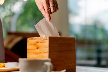 Kâğıt peçeteyi ahşap bir kutuya koyan bir el, kafenin arka planı bulanık. Amaç, peçeteden kurtulup temiz bir sayfa açmak.