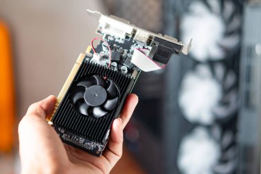 Elinde siyah vantilatörlü bir grafik kartı olan bir kişi bileşenlerini sergiliyor. Arka planda görünür soğutma vantilatörleri olan bir bilgisayar çantası var.