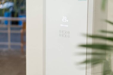 Modern bir klima ünitesinin, 23 derecelik bir dijital sıcaklık ölçümünü gösteren yakın çekim görüntüsü. Birim, kontrollü, gösterişli, minimalist bir tasarıma sahip.