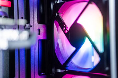 RGB ışıklandırmalı, canlı renkler gösteren ve karmaşık tasarımı olan bir bilgisayar vakası hayranının yakın çekim görüntüsü. Vantilatör, modern bir bilgisayar kurulumu içinde yer almaktadır.
