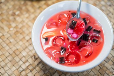 İçinde jöle halkaları, meyve parçaları ve tatlı kırmızı bir şurupta çikolata parçaları olan renkli bir tatlı kasesi. Bir kaşık tatlının birazını kepçeleyecek, canlı c 'sini gösterecek.