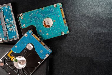 Karanlık bir yüzeydeki birkaç sabit disk sürücüsünün (HDD 'lerin) yakın görüntüsü. Görüntü sürücülerin karmaşık devre kartlarını ve mekanik bileşenlerini gösterir, vurgular