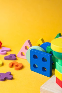 Geometrik şekiller ve parlak sarı arkaplandaki rakamlar da dahil olmak üzere ahşap eğitici oyuncaklardan oluşan renkli bir düzen. Oyuncaklar çocukların öğrenme ve oyun deneyimlerini geliştirmeleri için tasarlandı.