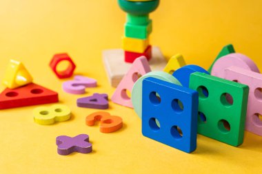 Parlak sarı bir zemin üzerinde ahşap geometrik şekiller ve rakamlardan oluşan renkli bir çeşitlilik. Şekiller çeşitli renklerde üçgenler, daireler, kareler ve altıgenler içerir.