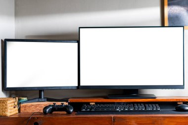 Ahşap bir masada boş ekranları olan çift bilgisayar monitörleri, bir klavye ve bir oyun denetleyicisi eşliğinde..