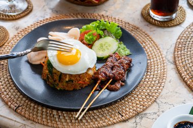 Yanında fıstık soslu şiş, salatalık dilimleri, marul ve karides krakerleriyle servis edilen, güneşte pişmiş yumurtalı bir tabak pilav..