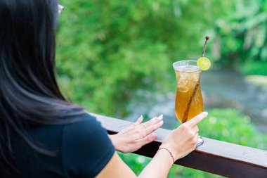 Uzun bir bardak limonlu buzlu çayı, yemyeşil arka planda tutan biri. İçki limon ve karıştırıcı ile süslenir, ferahlatıcı bir yaz havası yaratır..