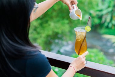 Uzun bir bardak limonlu buzlu çayı, yemyeşil arka planda tutan biri. İçki limon ve karıştırıcı ile süslenir, ferahlatıcı bir yaz havası yaratır..