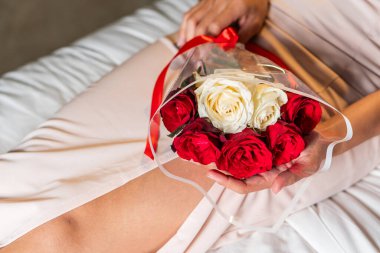 A close-up of a person holding a bouquet of red and white roses. The person is wearing a light-colored dress, and the bouquet is wrapped in a clear plastic cover. The setting appears to be indoors clipart