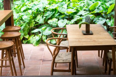 Ahşap bir masa ve yemyeşil yapraklarla çevrili sandalyelerin bulunduğu rahat bir açık hava yemek alanı. Ortam sakin ve davetkar, doğada yemekten zevk almak için mükemmel..