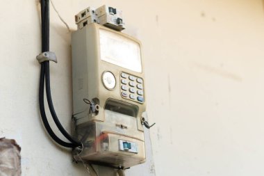 Eski, yıpranmış bir elektrik sayacı bir duvara monte edilmiş, içinde tuş takımı ve ekran var. Taksimetre, solmuş dış ve görünür bir giysi ile yaş belirtileri gösteriyor..