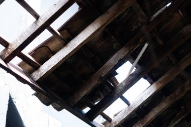 Kırsal ahşap çatı yapısının yakın çekim görüntüsü, görünür aşınmış kirişler ve kalaslar. Işık boşluktan süzülüyor, tahtanın dokusunu vurguluyor..