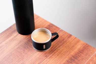 Siyah bir termos ve kahve dolu bir fincan ahşap bir masaya konur..