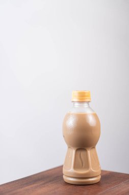 Kahverengi sıvı içeren sarı kapaklı plastik bir şişe, ahşap bir yüzeye yerleştirilmiş..