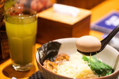 Kaynamış yumurta, deniz yosunu ve yeşil sebzeli bir kase r amin, yanında da ahşap bir masada bir bardak yeşil çay..