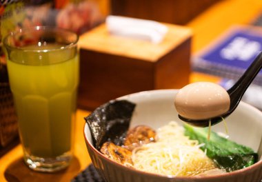 Kaynamış yumurta, deniz yosunu ve yeşil sebzeli bir kase r amin, yanında da ahşap bir masada bir bardak yeşil çay..