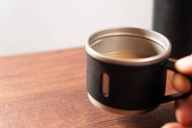 Tahta bir masada siyah bir fincanda dumanı tüten bir kahve fincanı..