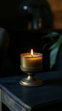 Ahşap bir masada, arka planı bulanık dekoratif bir tutacakta yanan bir mum. Ateşin sıcak parıltısı sıcak bir atmosfer yaratır..