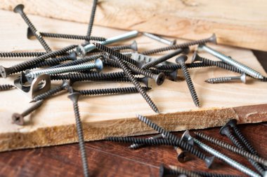 A scattered assortment of screws and nails on a wooden surface, showcasing various types and sizes. The background features a piece of wood, enhancing the workshop atmosphere. clipart