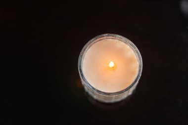 Cam kavanozdaki yanan bir mumun yakın plan görüntüsü, karanlık bir arka plana sıcak bir ışık saçıyor..