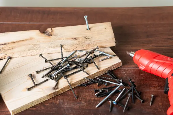 Tahta bir yüzeye saçılmış bir vida koleksiyonu ve yanında da matkap var. Bazı vidalar kısmen ahşap bir tahtanın içine gömülüdür, bir YID veya inşaat seti sergilerler..