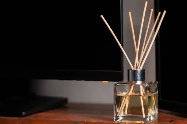 Ahşap kamışlı şık bir cam difüzyon koyu renkli bir monitörün yanındaki ahşap bir yüzeye oturur ve rahatlatıcı bir atmosfer yaratır..