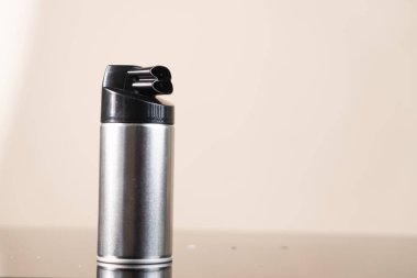 Pürüzsüz, gümüş bir sprey kutusuyla siyah bir başlık, yansıtıcı bir yüzeye yerleştirilmiş..